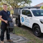 Rectify Plumbing plumber on Epping NSW footpath with CCTV drain camera reel and branded ute — blocked drain council responsibility specialist