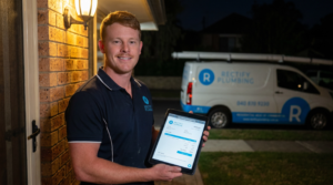Emergency plumber arriving at Epping NSW home at night holding fixed price quote on tablet