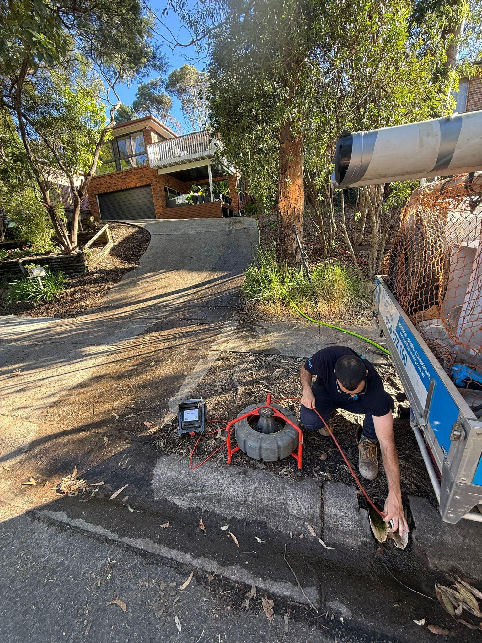 Drain cleaning machine set up on a driveway beside a Rectify Plumbing ute while clearing a blocked sewer