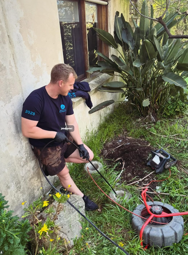Rectify Plumbing technician clearing a blocked stormwater gully in a Central Coast backyard