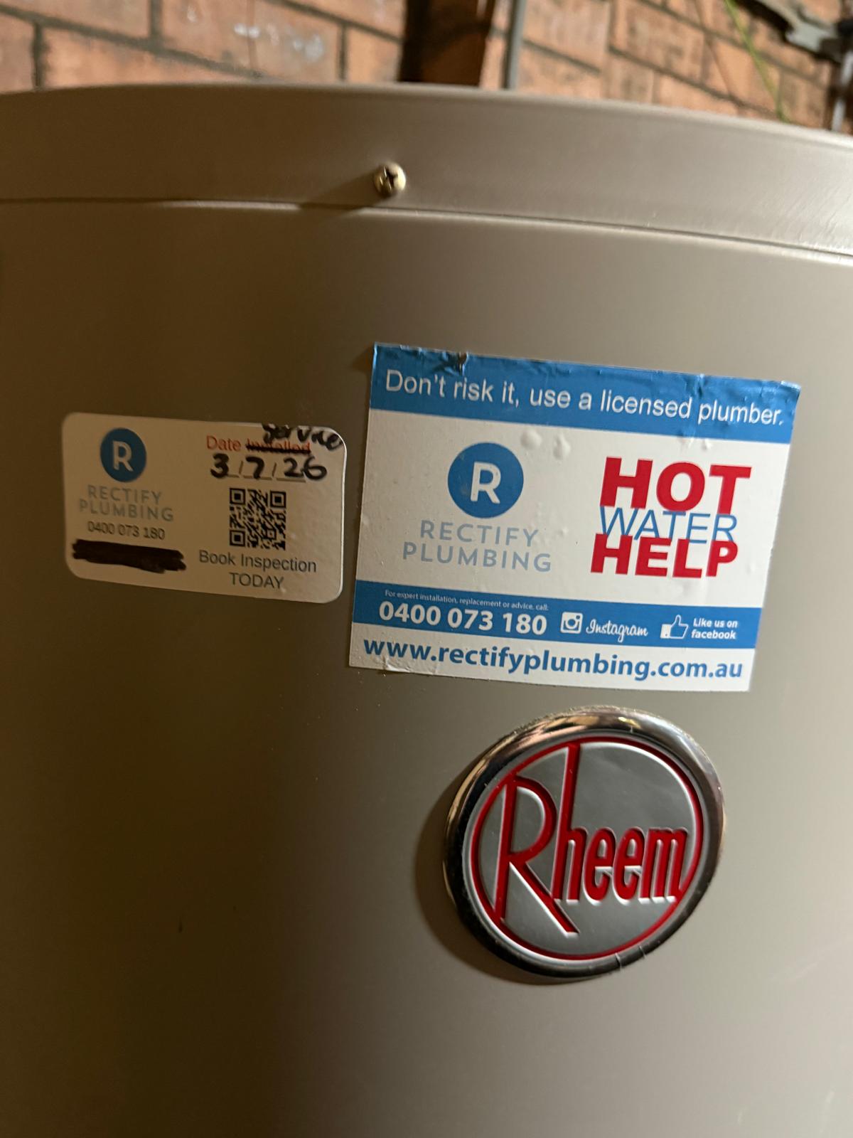Compliance sticker on a hot water unit reading do not risk it use a licensed plumber with the Rectify Plumbing phone number