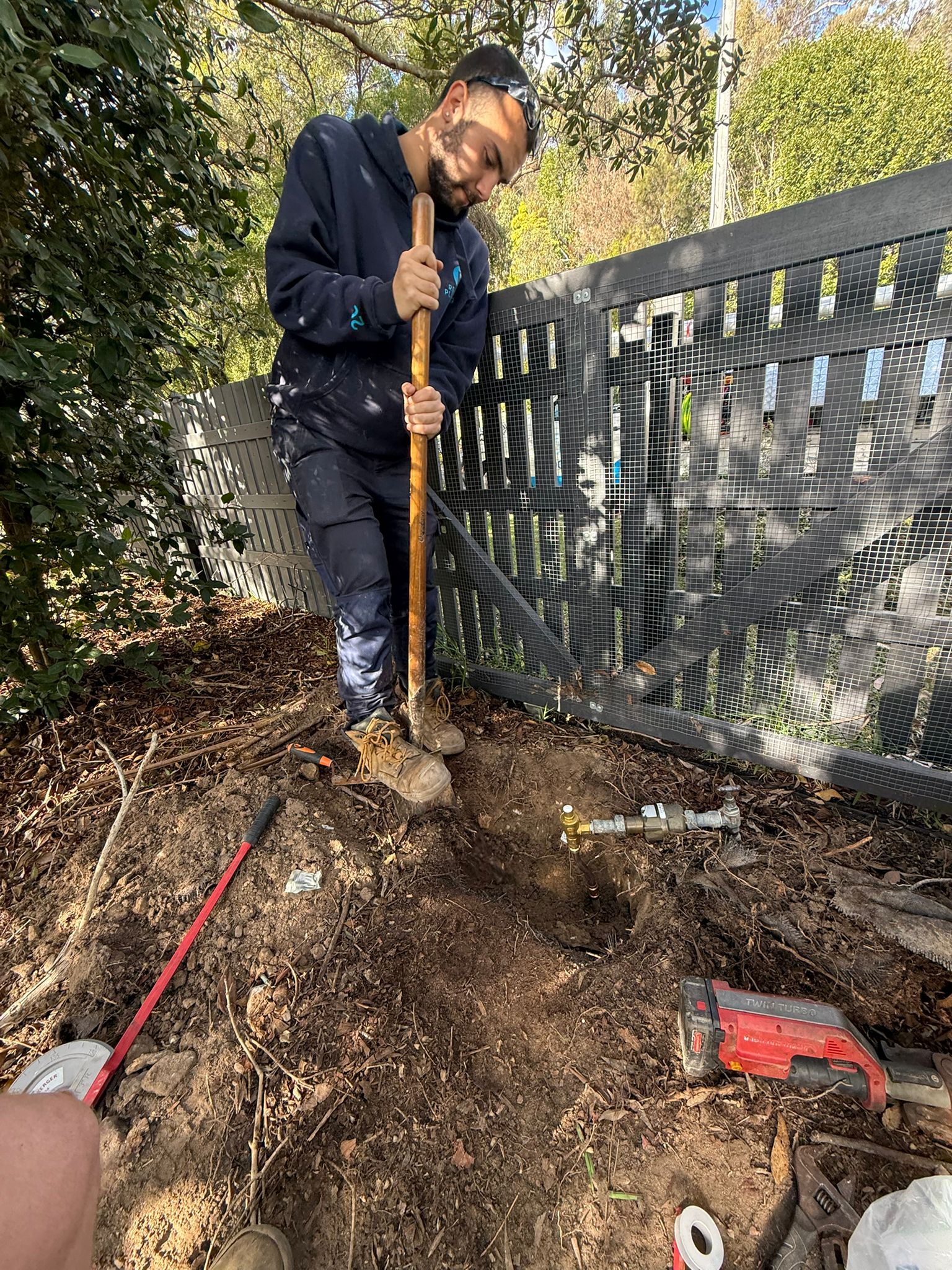 Rectify plumber digging in a backyard to expose and repair a blocked sewer pipe damaged by tree roots