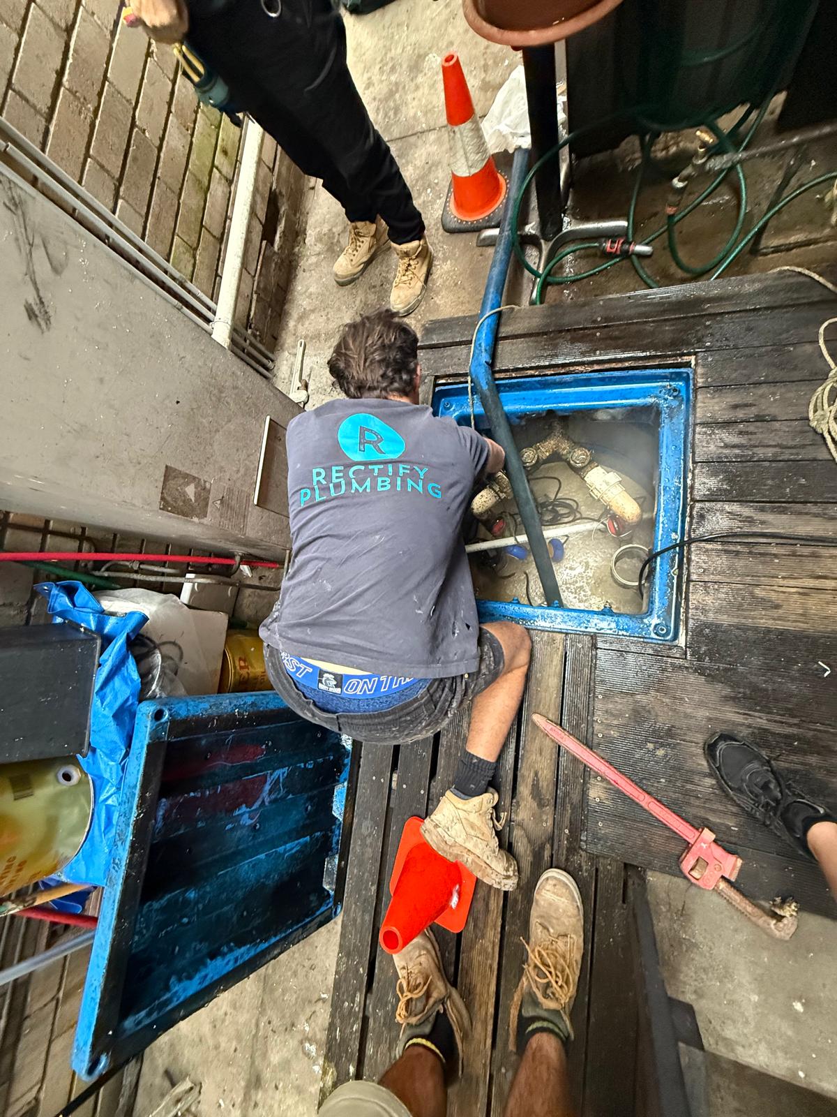 Rectify plumber working inside an open sewer inspection pit to clear a blocked drain near Gosford